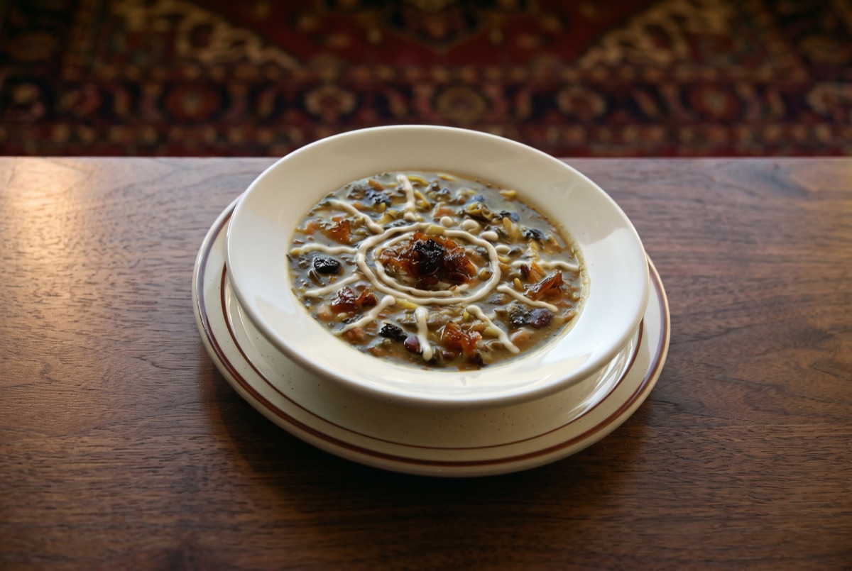 Ash Reshteh · Iran's beloved noodle soup, slow-simmered with herbs, beans, and lentils, topped with crisped mint oil and tangy…